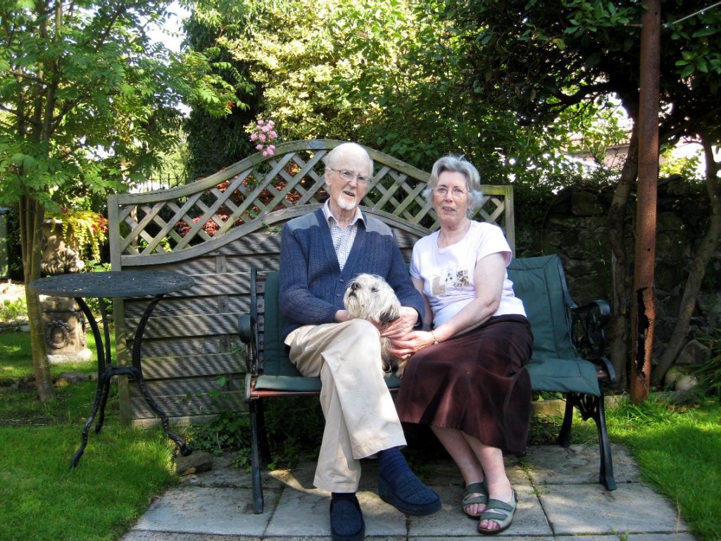 mum, dad, and Dandydinmont dog called Herbie sitting on a garden seat.