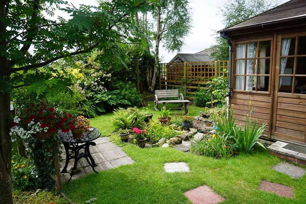 small garden with a summerhouse, seating and pond with slab stepping stones.